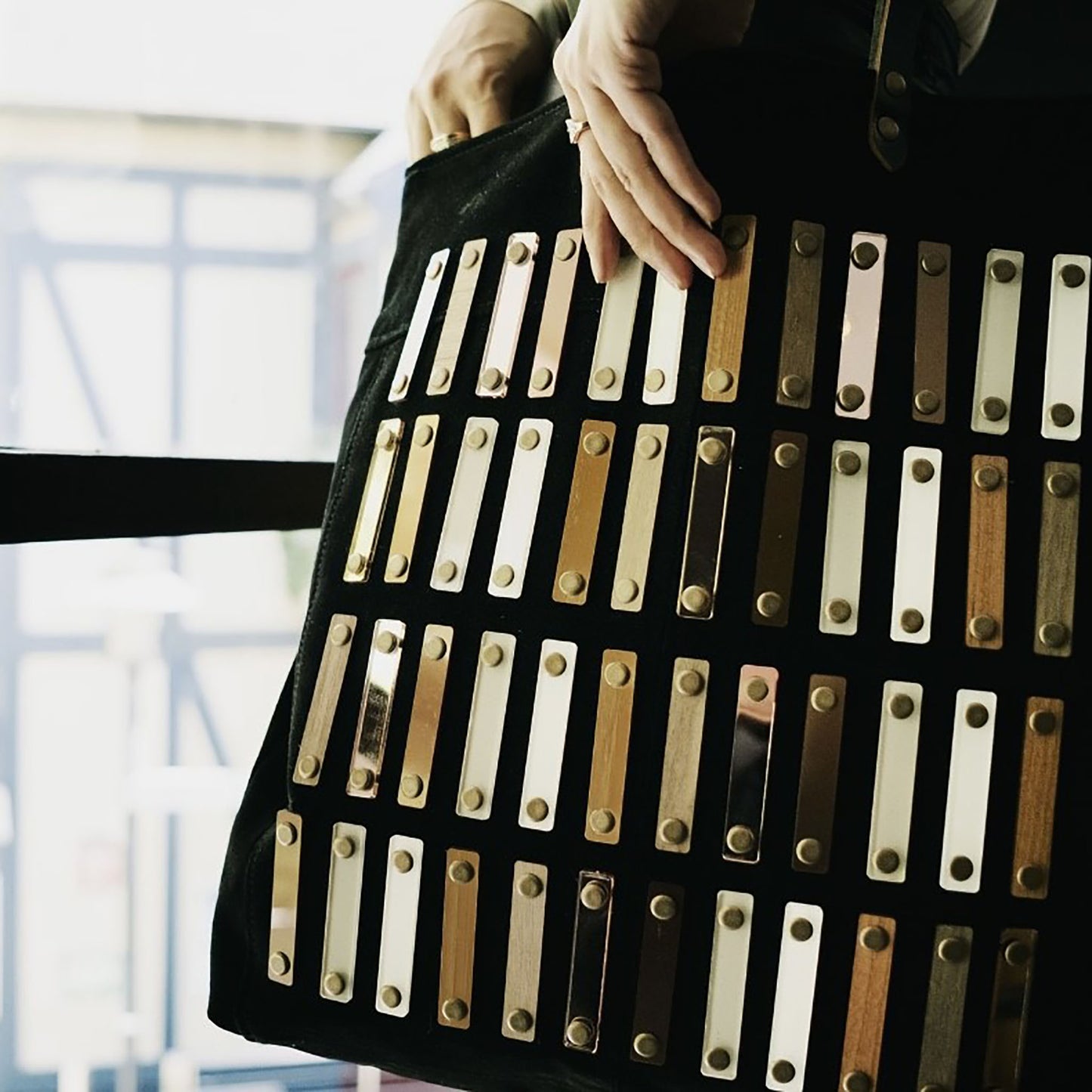 METANoIA black recycled leather tote handbag with acrylic and wooden vertical accents studded in a repeatitive fashion in an array of natural wooden browns, coppers and white. Featuring close up of the strokes tote.