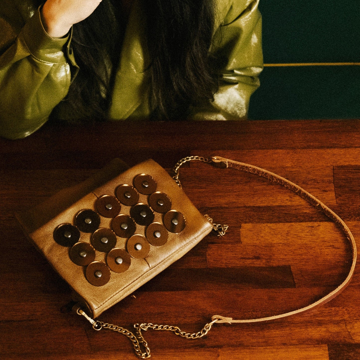 METANoIA tan recycled leather small handbag with circle copper acrylic forms fashioned into a repeative fashion with a smaller circle overlay on each form. Bag featured on a wooden table.