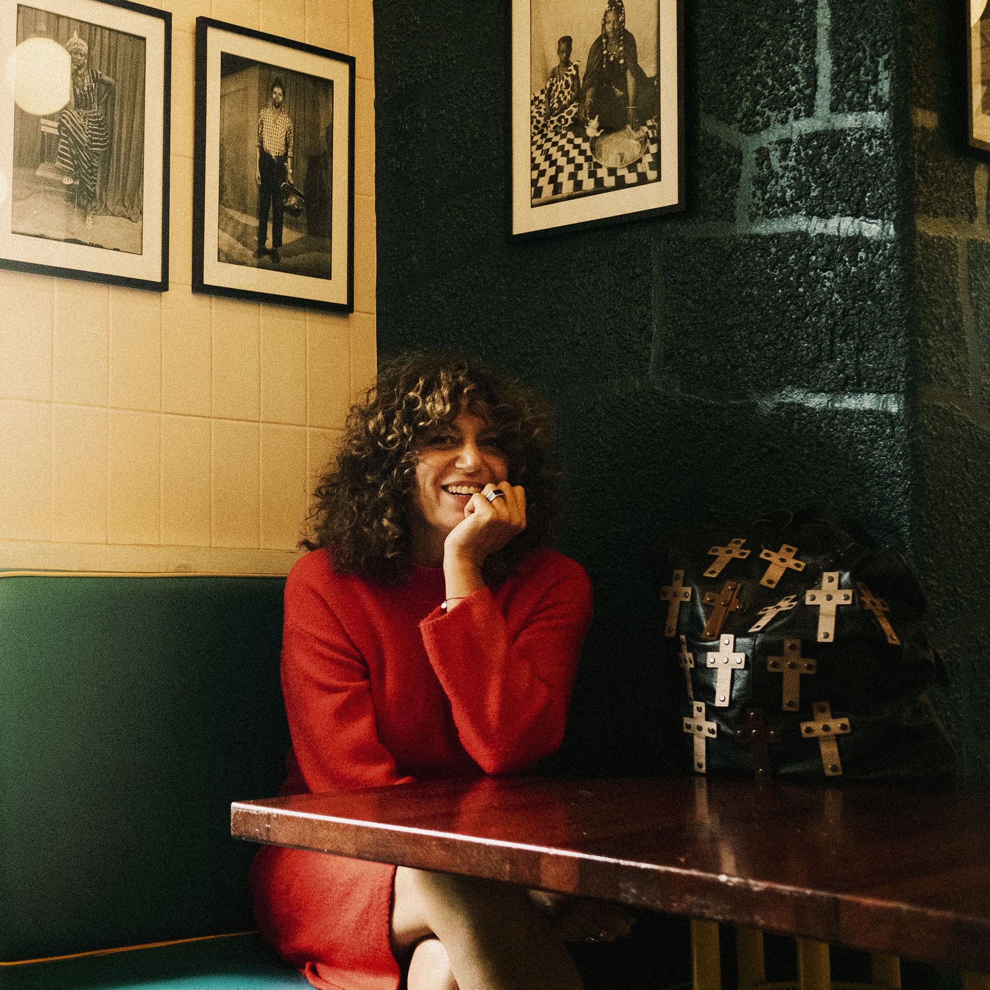 METANoIA The Cross Black recycled leather tote handbag with cross shaped bamboo, walnut and metallic acrylic forms. Model seated smiling with bag by her side.