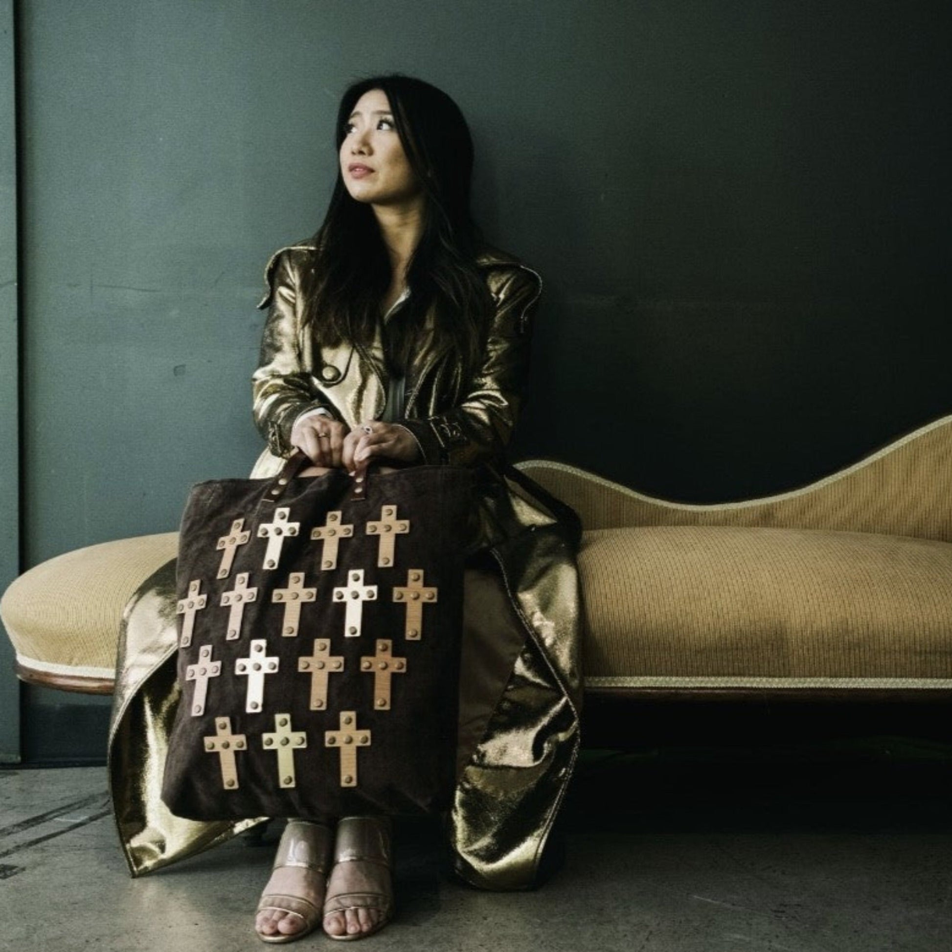 METANoIA The Cross Brown recycled leather tote handbag with cross shaped bamboo, walnut and metallic acrylic forms. Model featured browsing bag on a chaise lounge wearing a gold trench coat.