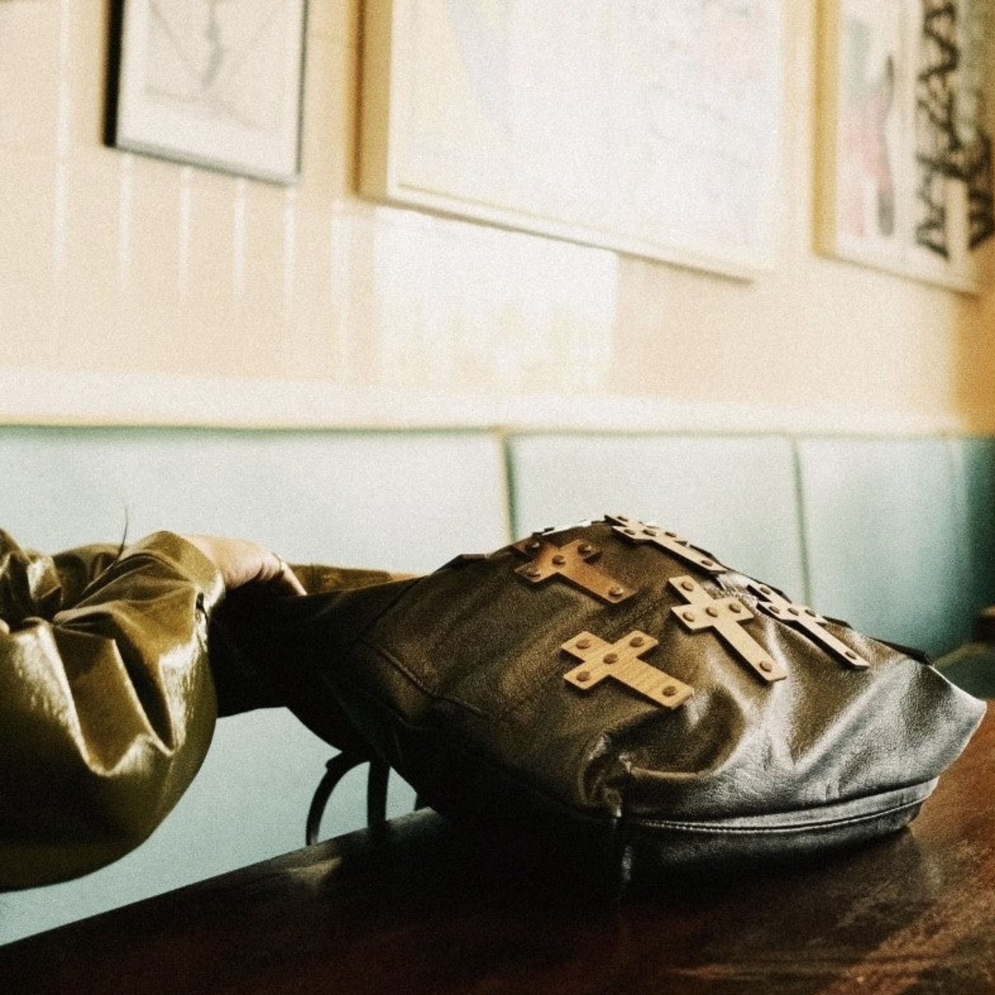 METANoIA The Cross Black recycled leather medium handbag with cross shaped bamboo, walnut and metallic acrylic forms with bag placed on a wooden restuarant table.