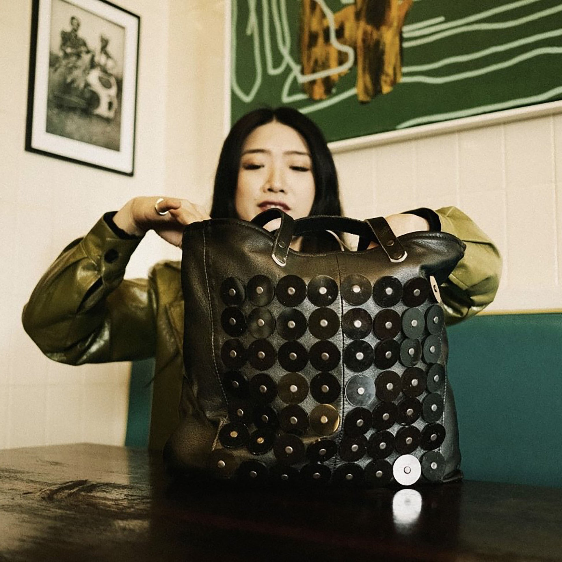 METANoIA black recycled leather medium handbag with black circle acrylic forms fashioned into a repeative fashion with a smaller circle overlay on each form.  Model shown looking into the disco bag.