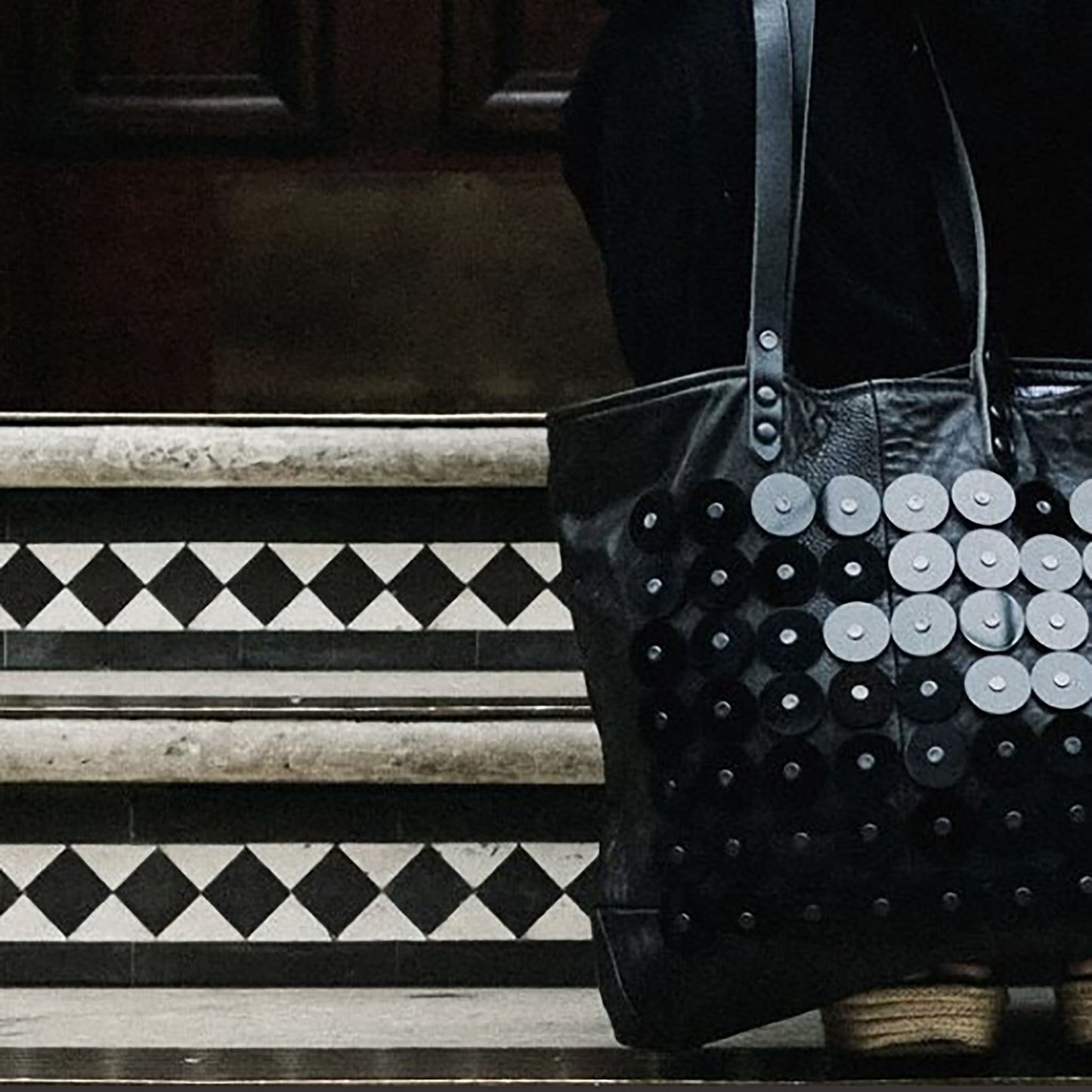 METANoIA black recycled leather medium handbag with black circle acrylic forms fashioned into a repeative fashion with a smaller circle overlay on each form. Close up on bag infront of geometric tiled stairs.