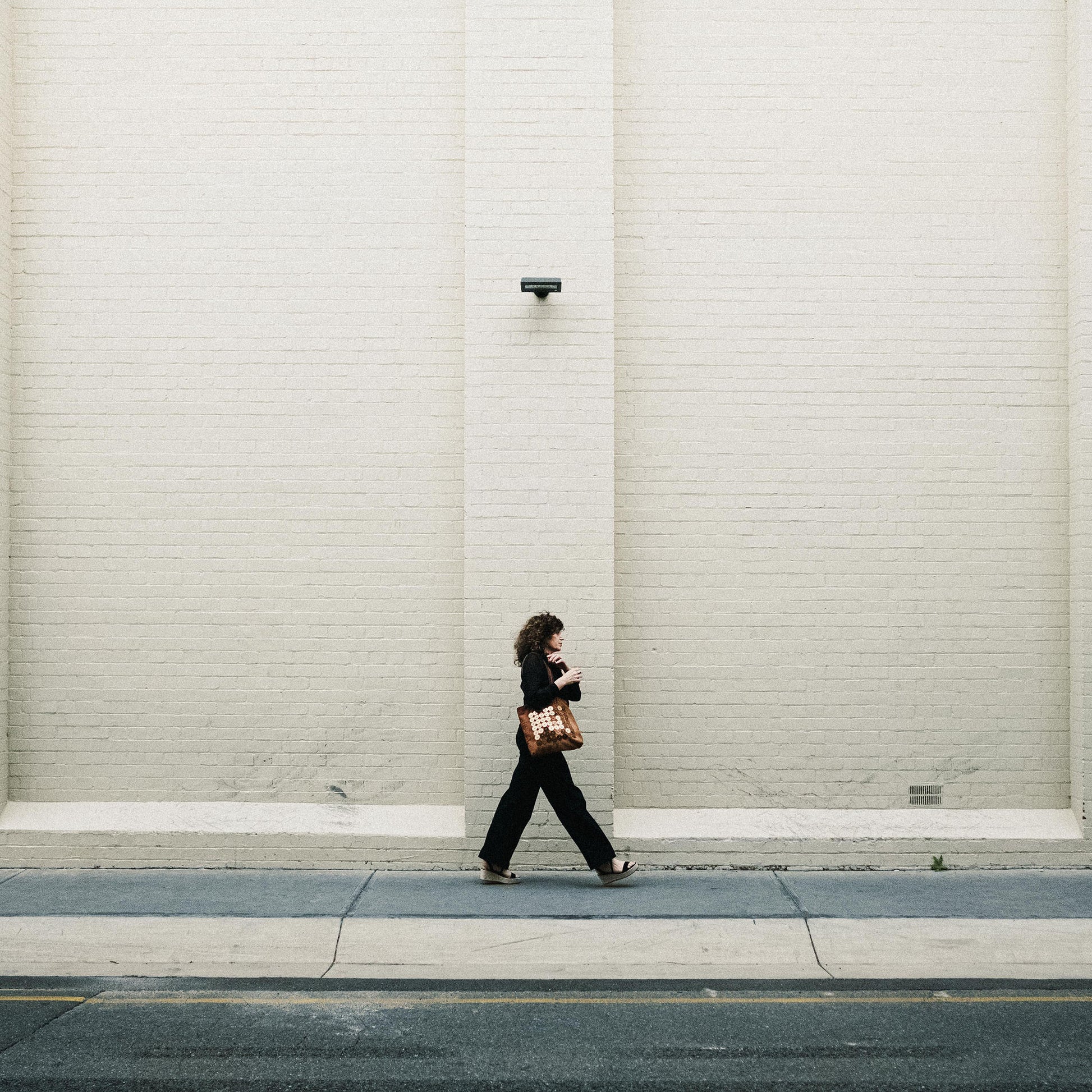 METANoIA tan recycled leather medium handbag with circle bamboo, walnut and acrylic forms fashioned into a repetitive fashion with a smaller circle overlay on each form. Model featured with bag walking across the street.