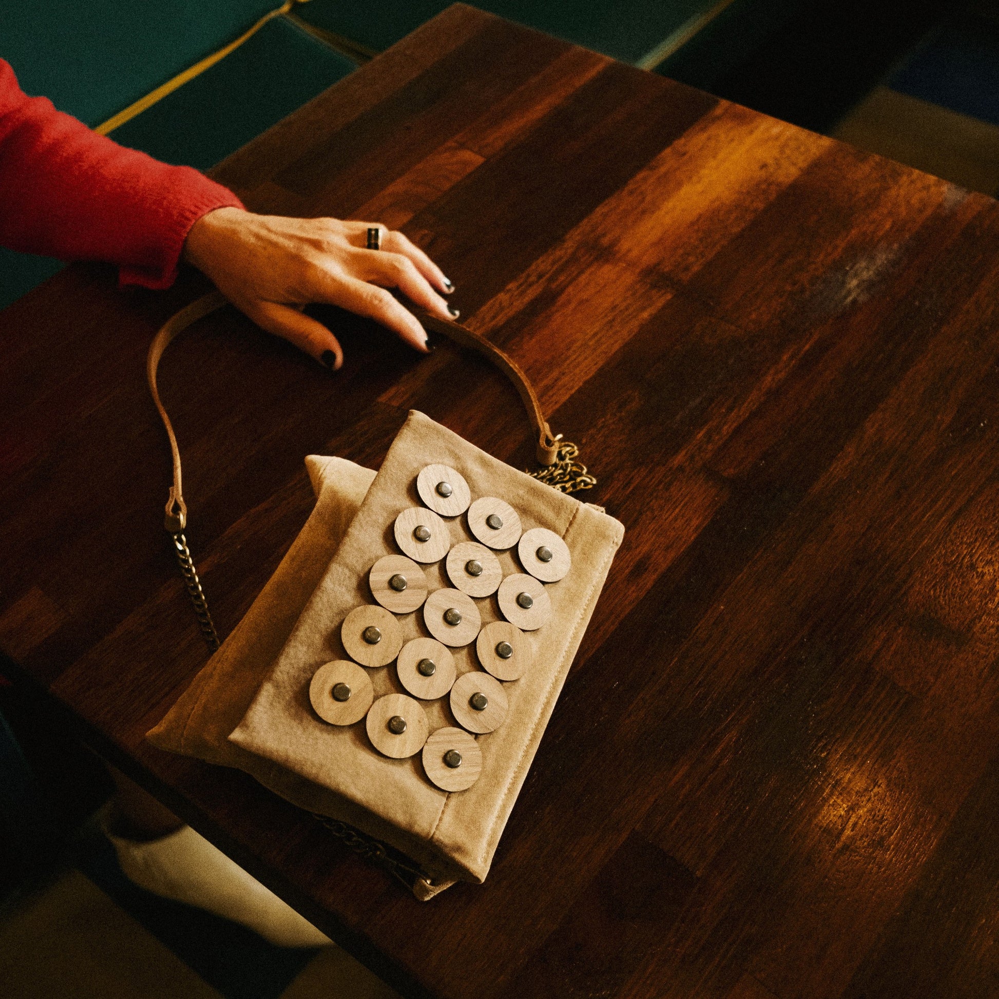 METANoIA tan recycled leather small handbag with circle bamboo and walnut acrylic forms fashioned into a repeative fashion with a smaller circle overlay on each form. Featured in birdseye view on a richly warm wooden table.