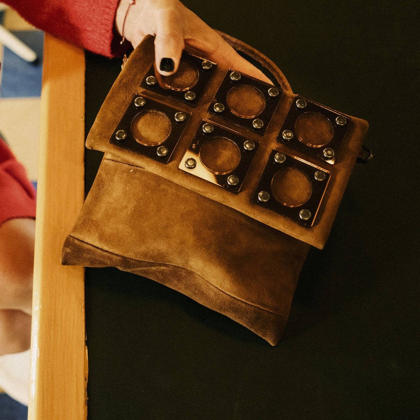 METANoIA tan recycled leather small handbag with square and hollowed circle bronze acrylic forms fashioned into a repeative fashion. Small bag placed on black and wood countertop.
