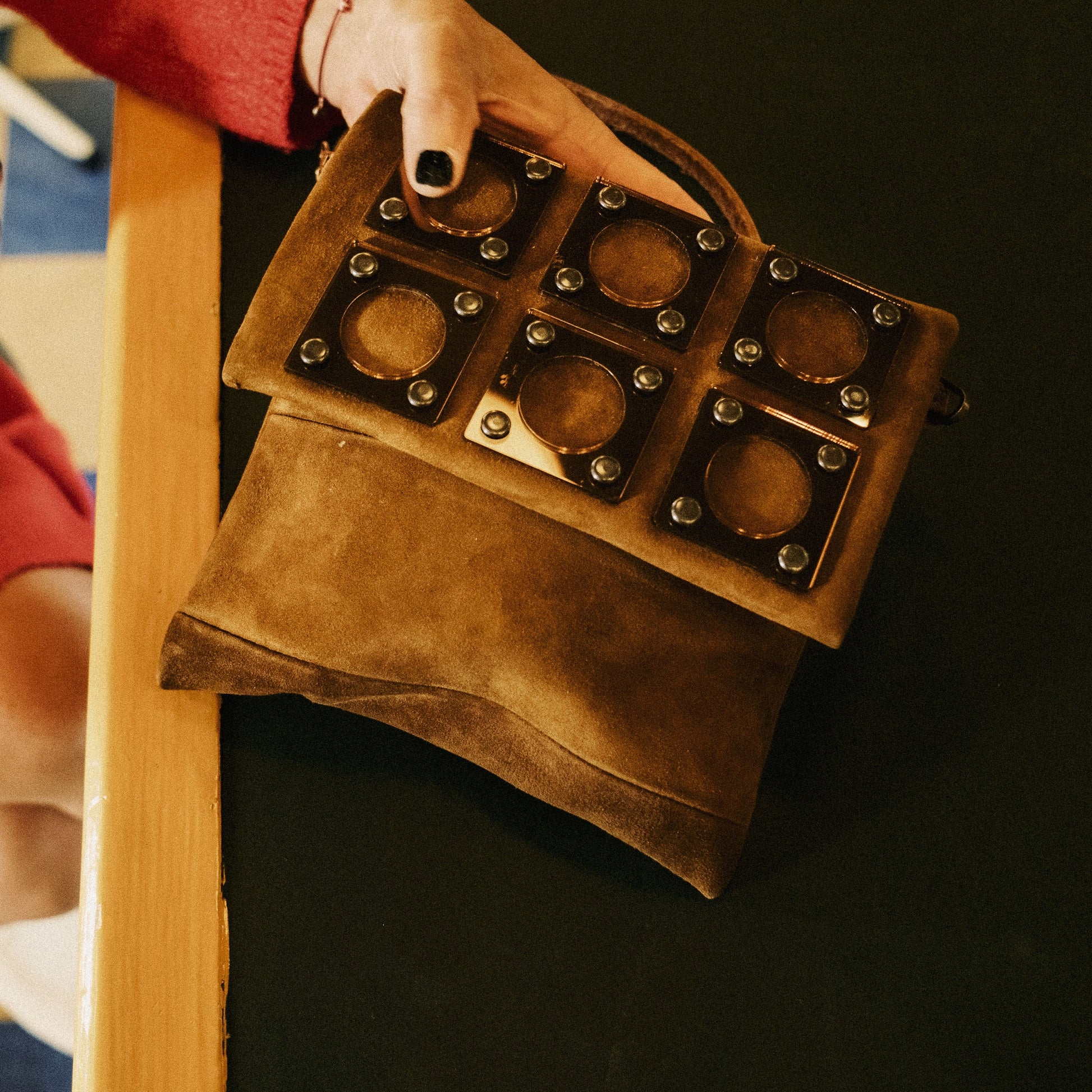 METANoIA tan recycled leather small handbag with square and hollowed circle bronze acrylic forms fashioned into a repeative fashion. Small bag placed on black and wood countertop.