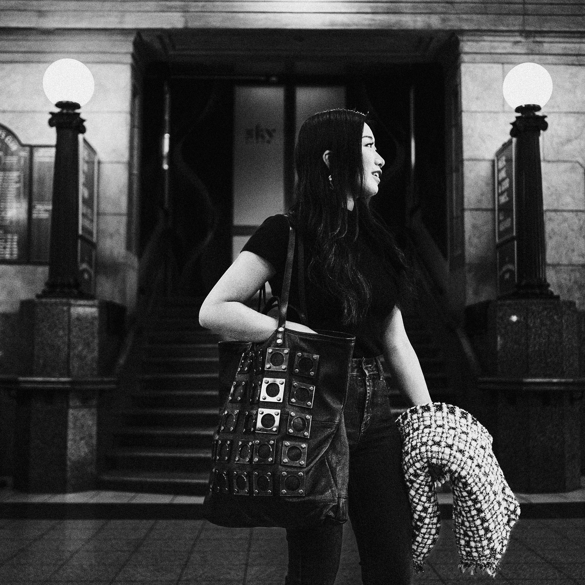 METANoIA black recycled leather tote handbag with square and hollowed circle bamboo and walnut acrylic forms fashioned into a repeative fashion. Model featured looking into distance with tote bag over her shoulder.