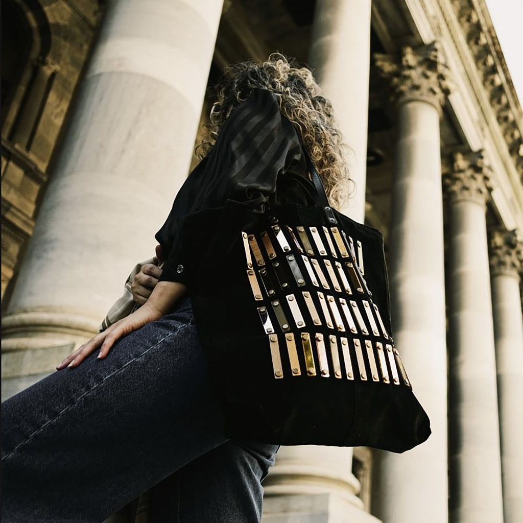 METANoIA black recycled leather tote handbag with acrylic and wooden vertical accents studded in a repeatitive fashion in an array of natural wooden browns, coppers and white.  Featuring model wearing the stroke bag over her shoulder.