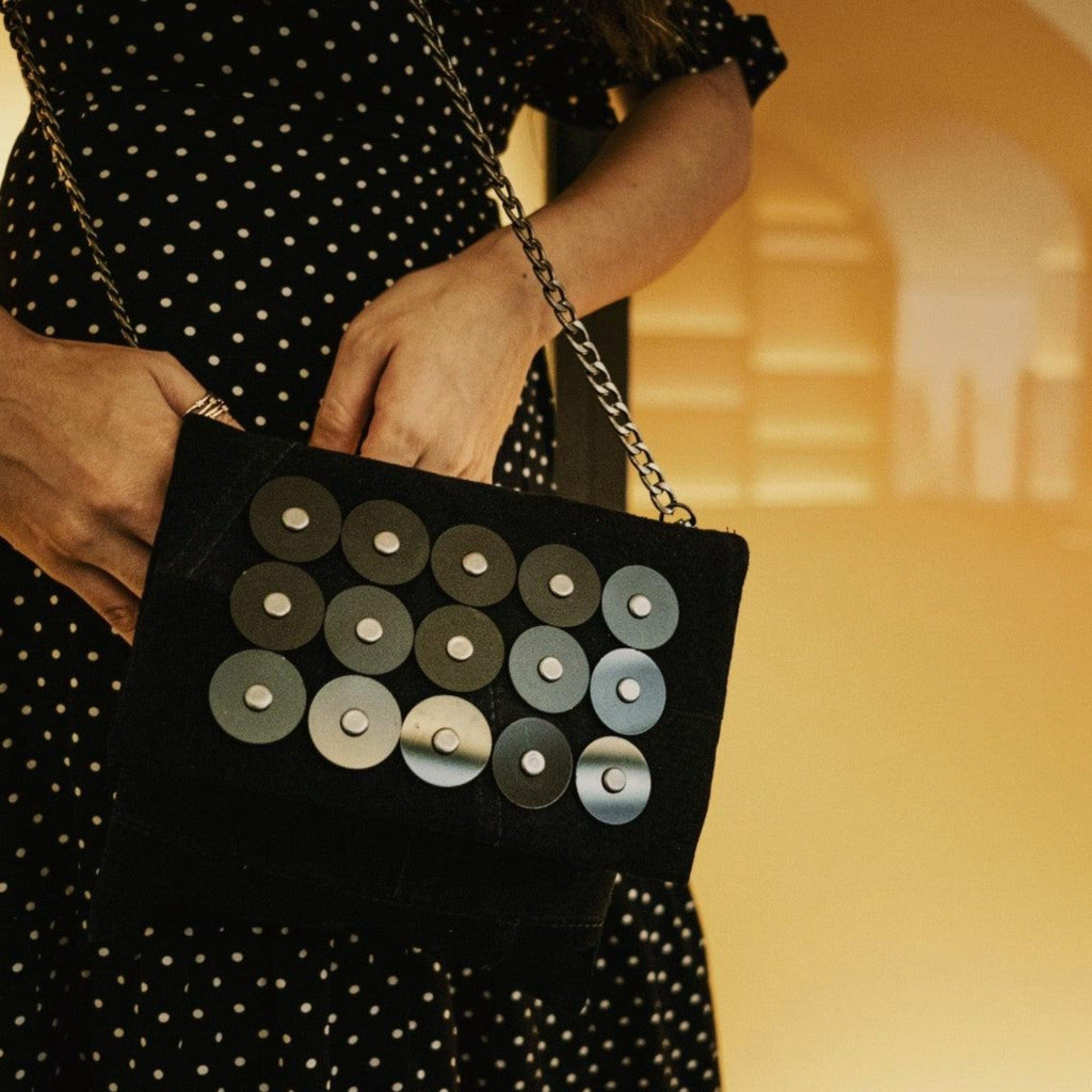 METANoIA black recycled leather small handbag with black circle acrylic forms fashioned into a repeative fashion with a smaller circle overlay on each form. Model featured in a polka dot dress with small disco bag infront of her.