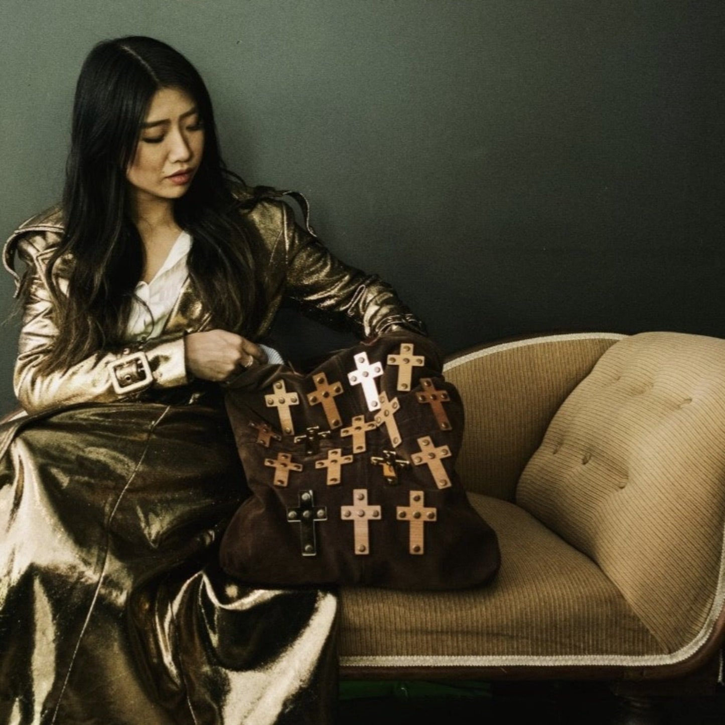 METANoIA The Cross Brown recycled leather tote handbag with cross shaped bamboo, walnut and metallic acrylic forms. Model featured browsing bag on a chaise lounge wearing a gold trench coat.