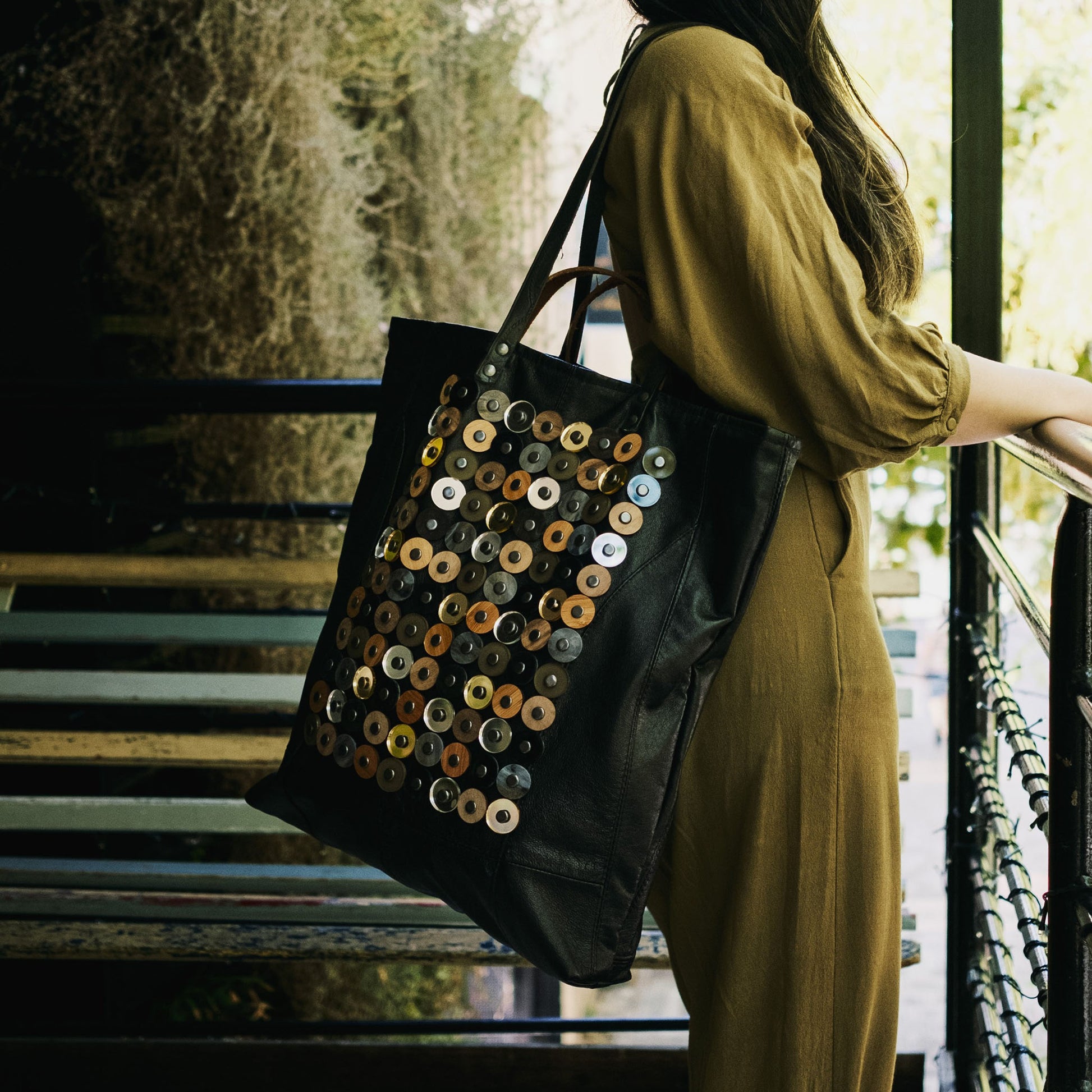 METANoIA black recycled leather tote handbag with  circle bamboo, walnut and acrylic forms fashioned into a repeative fashion with a smaller circle overlay on each form.  Model learning against balcony.